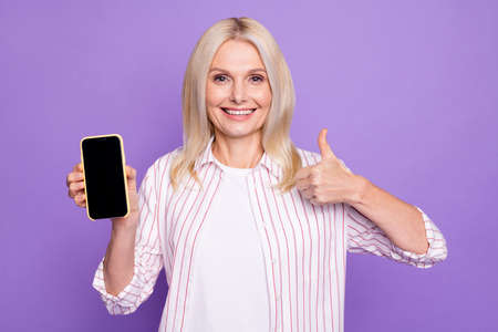 Photo of sweet lady pensioner wear striped shirt pointing modern device showing thumb up isolated...