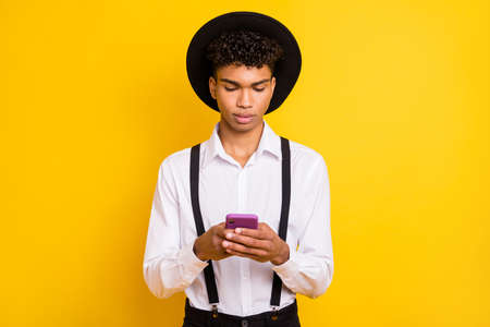 Photo portrait of african american man holding phone in two hands isolated on vivid yellow colored backgroundの写真素材