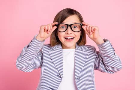 Portrait of attractive cheerful amazed intellectual girl learner touching specs isolated over pink pastel color backgroundの写真素材