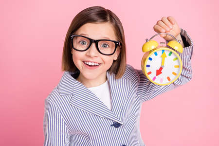 Portrait of attractive cheerful preteen girl learner holding in hands vintage clock early lesson...