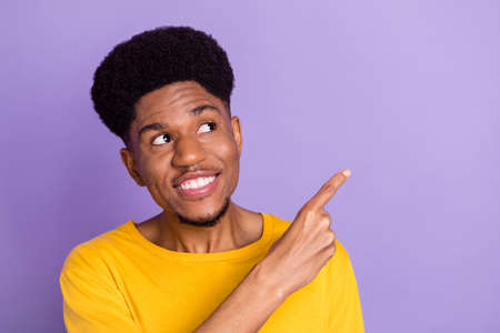 Photo of happy charming dark skin young man point finger empty space sale isolated on violet color...