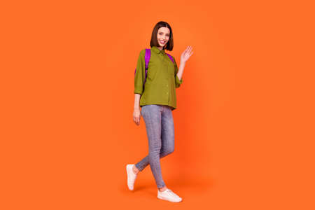 Full length photo of cute brunette young lady go wave wear bag shirt jeans isolated on orange color...