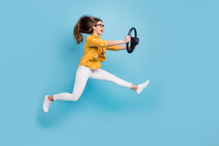 Full body profile side photo of young woman happy smile jump up ride speed steering-wheel taxi isolated over blue color backgroundの写真素材