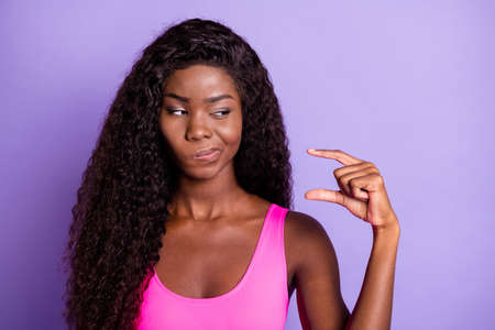 Photo of young african woman unhappy uncertain doubt look show fingers size isolated over violet color backgroundの写真素材