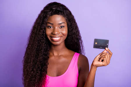 Photo portrait of african american woman holding credit card isolated on pastel pink colored backgroundの写真素材