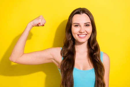 Portrait of attractive cheerful girl demonstrating strong muscles isolated over bright yellow color backgroundの写真素材
