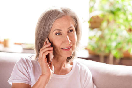 Photo of pretty charming lady pensioner wear white t-shirt sitting sofa smiling talking modern...