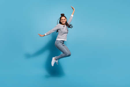 Full size profile side photo of young cheerful african girl happy positive smile have fun jump isolated over blue color backgroundの写真素材