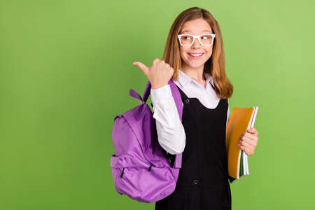 Portrait of attractive cheerful girl holding materials showing copy space ad isolated over green...
