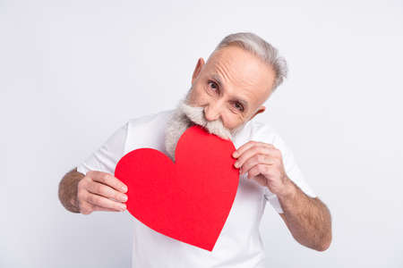 Photo of hungry old grandfather bite red paper big heart shape figure isolated on grey color backgroundの写真素材