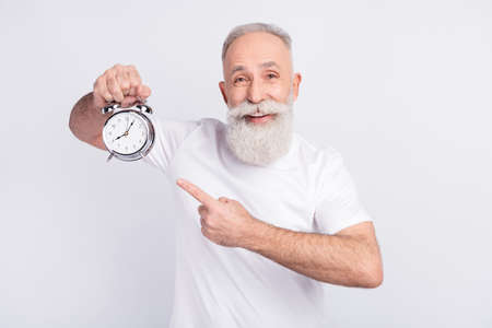 Portrait of attractive cheerful man holding in hand demonstrating vintage clock isolated over light...