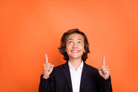 Photo of young dreamy cheerful little boy look point finger up solution news isolated on orange...