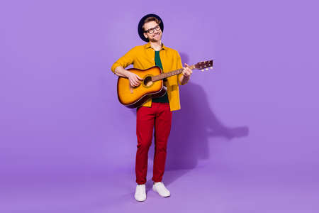Full body photo of creative happy positive young man look empty space play guitar isolated on violet color backgroundの写真素材