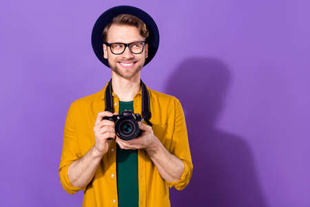 Portrait of nice cheerful curious guy holding in hands cam looking aside copy space isolated over bright violet purple color backgroundの写真素材