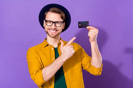 Photo of young guy happy positive smile indicate finger credit card recommend bank payment isolated over violet color backgroundの写真素材