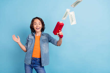 Photo of young boy happy positive smile hold gun shoot money rich dollars cash isolated over blue color backgroundの写真素材