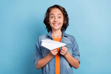 Photo of young preteen boy happy positive smile hold paper plane origami isolated over blue color backgroundの写真素材