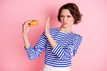 Portrait of young attractive disgusted negative girl look at hamburger hold hand no deny isolated on...