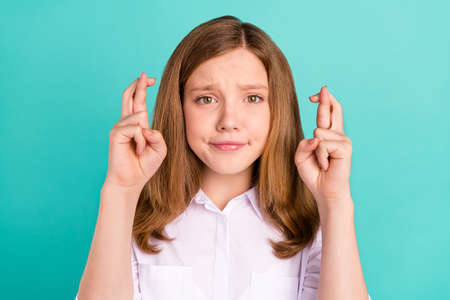 Portrait of attractive worried girl showing crossed fingers praying isolated over vibrant teal...