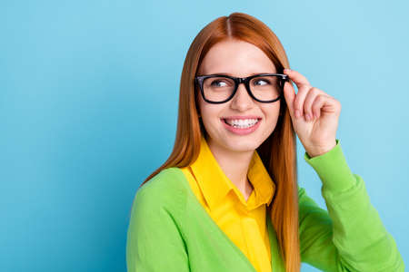 Photo of optimistic young lady look empty space wear spectacles yellow sweater isolated on blue...