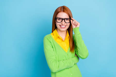 Photo of lovely young student lady touch spectacles wear green sweater isolated on blue color backgroundの写真素材