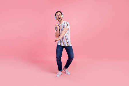Full body photo of cheerful young happy positive man wear headset dance enjoy isolated on pink color...