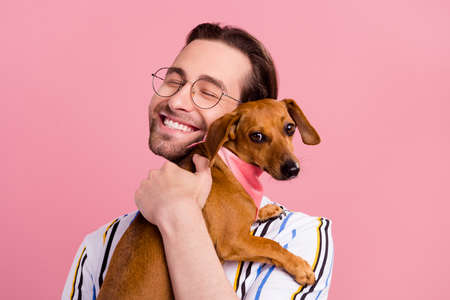 Photo portrait man in t-shirt glasses embracing brown puppy isolated pastel pink color backgroundの写真素材