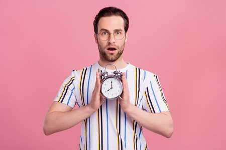 Photo of amazed shocked young man hold hands alarm clock late isolated on pastel pink color...