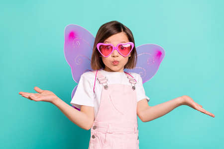 Photo of impressed puzzled schoolgirl dressed pink overall eyewear wings shrugging shoulders isolated turquoise color backgroundの写真素材