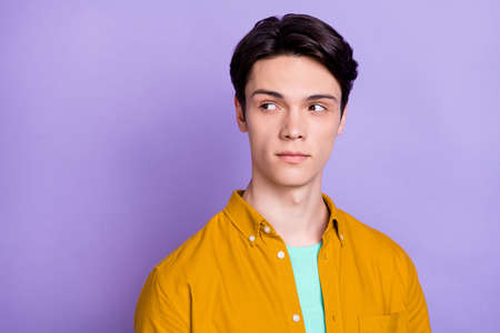 Photo of serious brunet young guy look empty space wear yellow shirt isolated on violet color...
