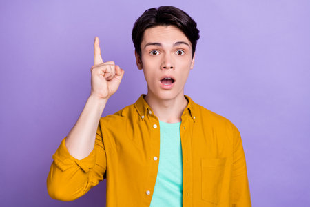 Photo of impressed brunet millennial guy point up wear yellow shirt isolated on violet color...