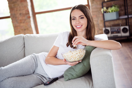 Photo of young attractive girl happy positive smile lying sofa watch cinema comedy eat pop corn indoorsの写真素材