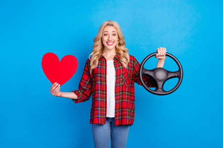 Photo of charming sweet young lady wear plaid shirt holding steering wheel red heart smiling isolated blue color backgroundの写真素材