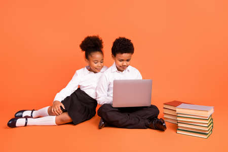 Full size photo of two young afro school kids classmates make homework computer isolated over orange color backgroundの写真素材