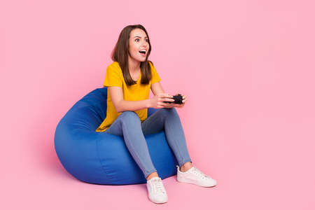 Photo of cute excited woman dressed yellow t-shirt sitting while looking empty space isolated pink color backgroundの写真素材