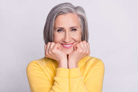 Portrait of mature beautiful lovely sweet grandmother smiling admiring hold hands chin isolated on grey color backgroundの写真素材
