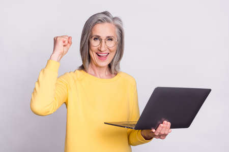 Photo of happy excited cheerful businesswoman hold laptop raise fist in victory isolated on grey color backgroundの写真素材
