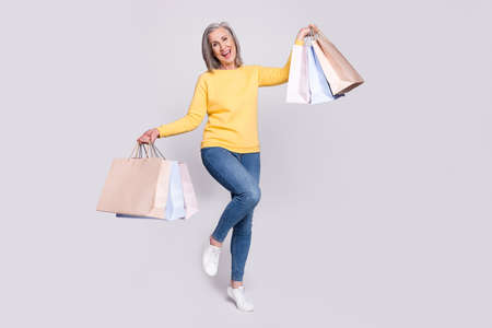Full size photo of happy excited lovely grandmother shopaholic hold bags isolated on grey color...