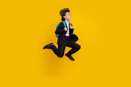 Profile photo of carefree small boy jump run wear rucksack black uniform isolated yellow color backgroundの写真素材