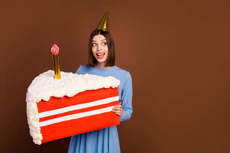 Photo of impressed young brunette lady hold cake wear hat blue dress isolated on brown color...