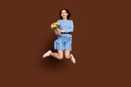 Full length photo of funny brunette lady jump with flowers wear blue dress isolated on brown backgroundの写真素材