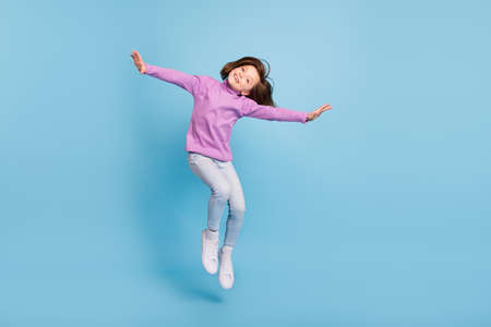 Photo of pretty charming school girl wear purple turtleneck jumping high smiling isolated blue color...
