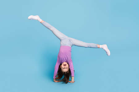 Full length body size photo little girl doing handstand overjoyed isolated pastel blue color...