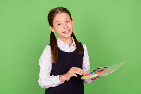 Photo of young school girl happy positive smile draw picture artwork lesson isolated over green color backgroundの写真素材