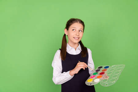 Photo portrait schoolgirl keeping color palette with paint brush looking copyspace isolated pastel green color backgroundの写真素材