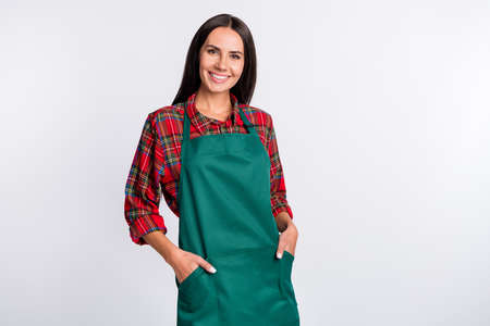 Photo of lovely positive young woman hold hands green apron pocket smile work barista isolated on grey color backgroundの写真素材