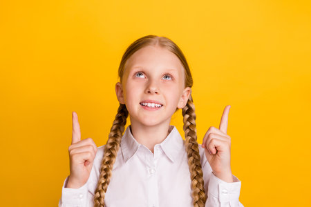 Photo of positive pupil look direct finger above empty space beaming smile isolated on yellow color...