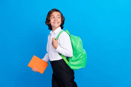 Photo of pretty funny schoolboy wear formal clothes rucksack holding book walking looking empty space isolated blue color backgroundの写真素材