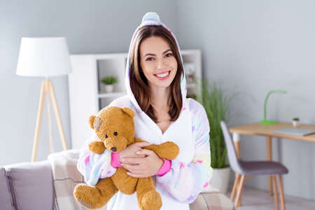 Photo of sincere genuine winsome candid adorable lady cuddle toy bear wear unicorn cosplay kigurumi indoorsの写真素材