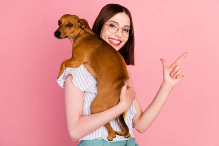 Photo of sweet brunette young lady hold dog point empty space wear eyewear white blouse isolated on pink color backgroundの写真素材